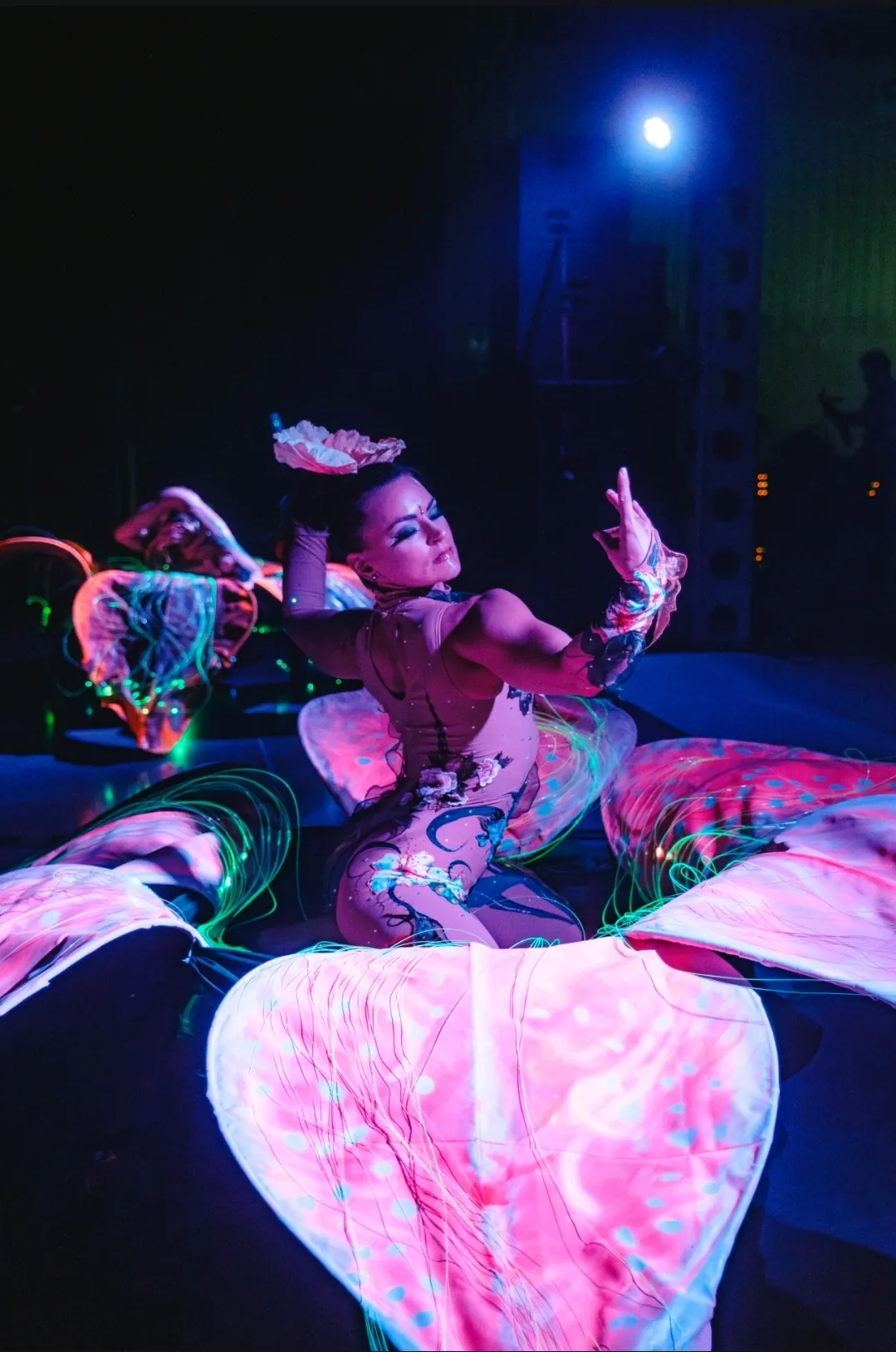 Contortionist in a glowing fiber optic flower costume under UV light