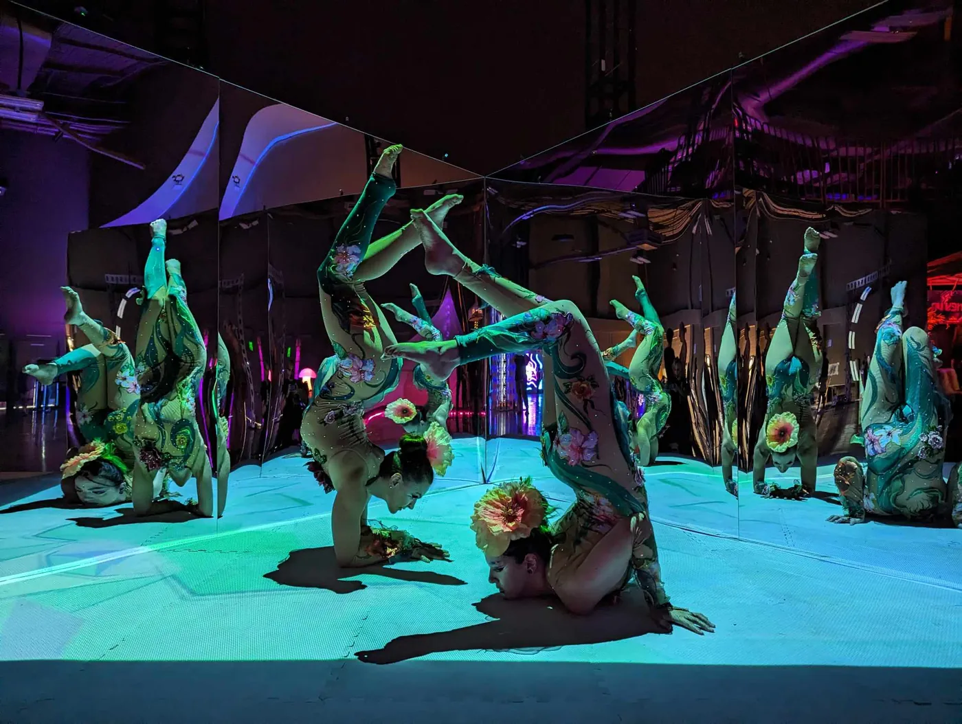 Two contortionists in flower costumes on the projected floor of The Compendium, reflected in the mirrors