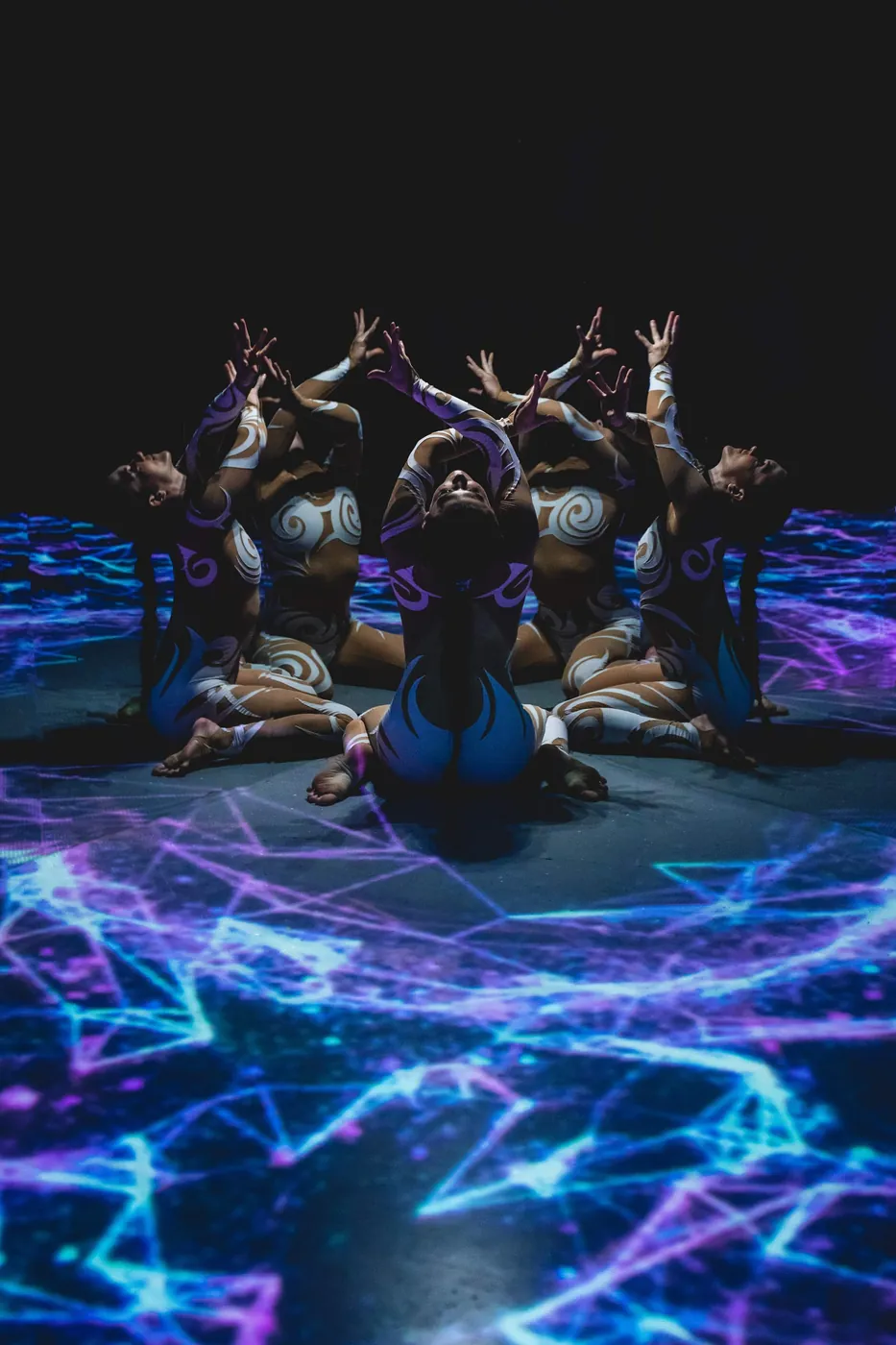 Contortionists posed together over the glowing projected floor of The Compendium