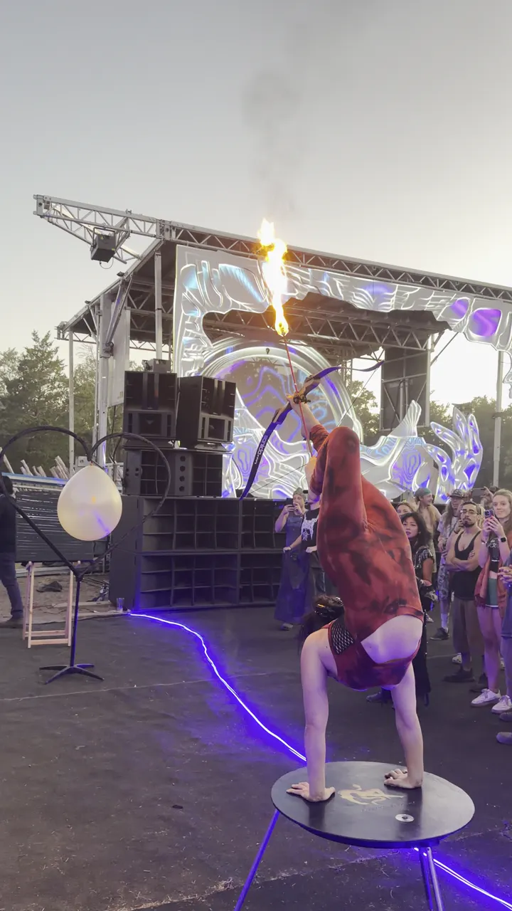 Contortionist firing a flaming arrow from a handstand on a portable table